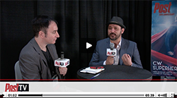 Two men sit at a table with microphones during a PostTV interview against a black backdrop.