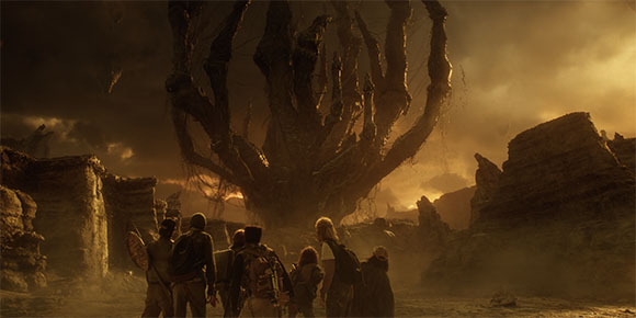 A group of people viewed from behind, looking up at a giant, dark, multi-limbed tree in a dusty, golden landscape.
