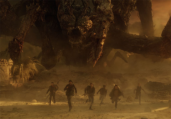 A massive, dark, multi-legged monster towers over several people running across a dusty landscape.