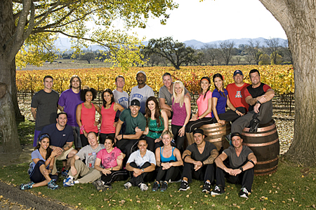 A diverse group of people smiling and posing for a group photo in a vineyard with autumn foliage.
