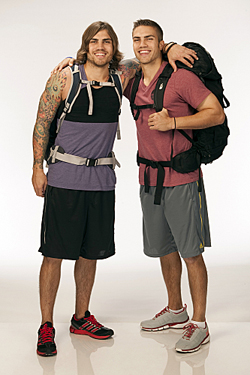Two smiling men standing side-by-side wearing athletic clothing and large backpacks against a white background.