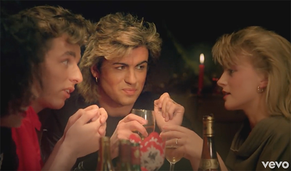 Three young people toast with glasses at a dark table lit by a single candle.