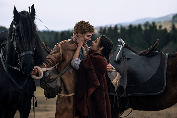 A man and woman embrace affectionately in a field next to two horses.
