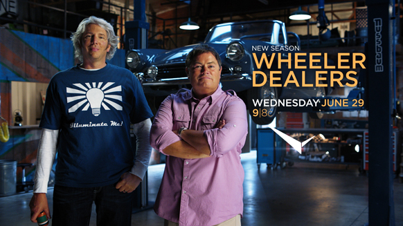 Two men stand in an auto shop in front of a classic blue car with show title text.