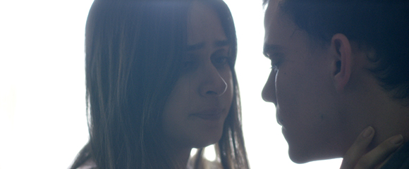 A woman with long hair looks intensely at a man's face in a close-up shot.