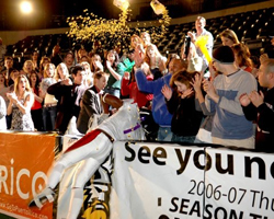 A large crowd of people cheering and clapping as gold confetti falls over them in a stadium.