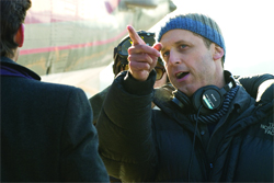 A man wearing a blue beanie and headphones points his finger while speaking to someone off-camera.
