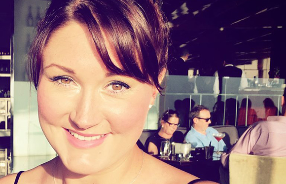 A smiling woman with dark hair and brown eyes looking at the camera in a restaurant setting.