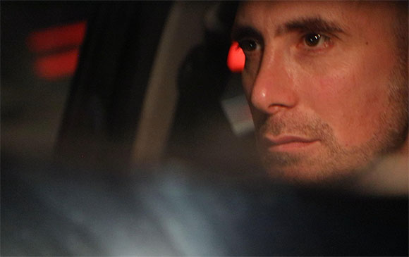 A close-up profile of a man looking forward in dim, warm lighting.