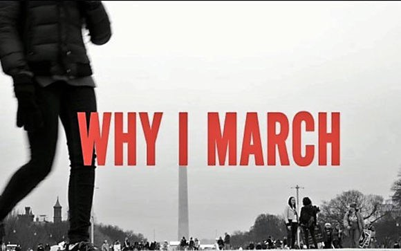 A person stands in the foreground before a crowd and a tall monument with red text reading 'WHY I MARCH'.