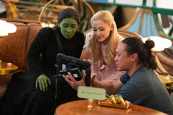 A green-skinned woman, a blonde woman, and a man look at a tablet screen together.