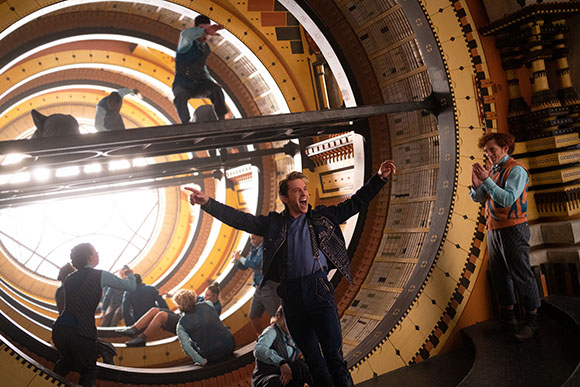 People stand and move within a large, circular structure with golden, tiered levels.