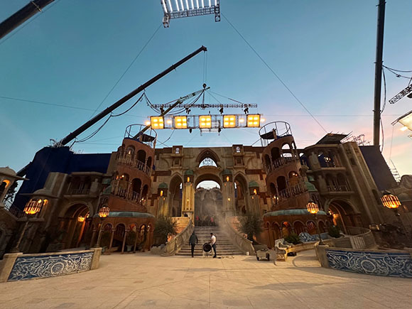 A large, multi-story Mediterranean-style film set with arches and balconies under a blue twilight sky.