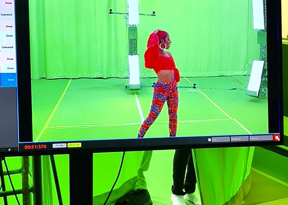A person in a red top and colorful patterned leggings stands in a green screen studio.