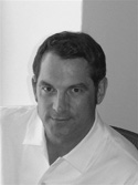 Black and white portrait of a man with dark hair wearing a white collared shirt.