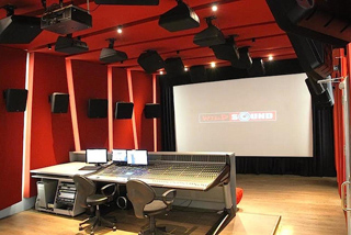 A sound mixing studio featuring red acoustic walls, a large mixing console, and a projection screen.
