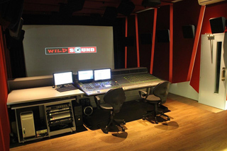A recording studio featuring a large mixing console, computer monitors, and a projection screen reading Wild Sound.