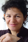 A smiling woman with dark curly hair rests her chin on her hand.
