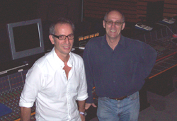 Two men wearing glasses and button-down shirts standing in front of a large mixing console.
