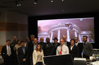 A group of people standing together in a dark room in front of a large screen showing a building.