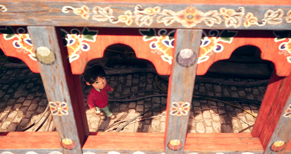 A small child in a red shirt looks up through a decorative, colorful wooden balcony railing.