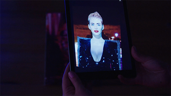 Hands holding a tablet showing a portrait of a woman with short blonde hair and red lipstick.