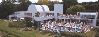 A large white modern building with curved roofs and a swimming pool crowded with people.