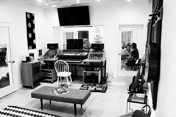 A music studio with mixing consoles, studio monitors, various instruments, and a white chair.