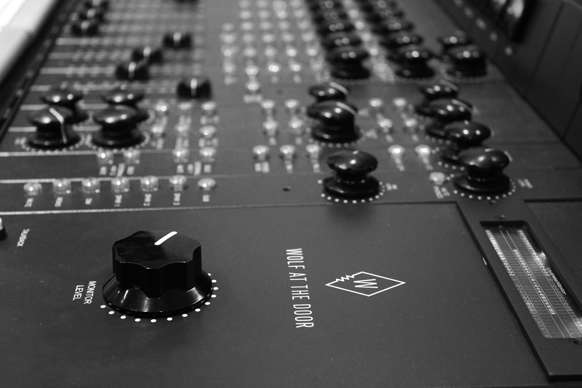 Close-up, low-angle view of a black audio mixing console with various knobs and sliders.