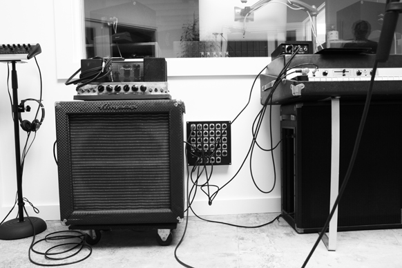 Black and white photo of a guitar amplifier, a mixer on a stand, and various audio equipment and cables.
