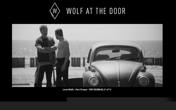 Black and white shot of two men standing near a vintage Volkswagen Beetle on a beach.
