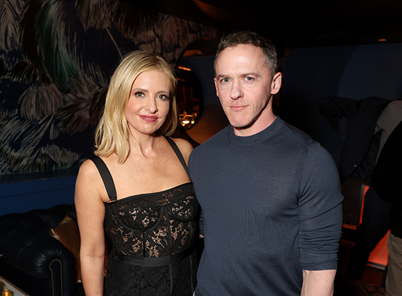 A blonde woman in a black lace dress and a man in a navy blue shirt standing side by side.