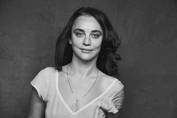 Black and white portrait of a woman with dark hair wearing a light-colored V-neck shirt and a necklace.