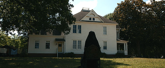 A large white two-story house with a gabled roof behind a dark silhouette of a person.