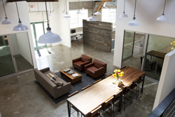 Aerial view of a modern office lounge with brown leather chairs, a sofa, and a long wooden dining table.