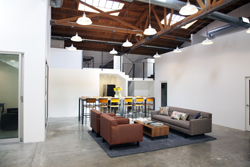 A spacious loft with high wooden beams, hanging pendant lights, a lounge area, and a long dining table.