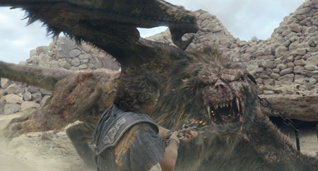 A man in ancient clothing holds a chain near the open maw of a large, furry, winged monster.