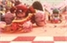 A large red character with large fists in a pink-toned, festive environment.