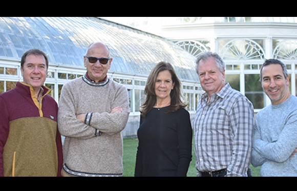 Five adults standing in a row outdoors in front of a large glass conservatory building.