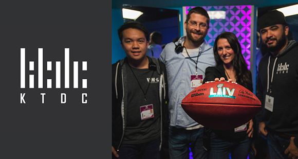 Four people smiling and posing together while holding a red football.