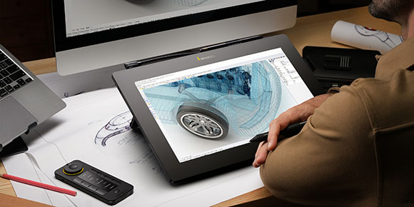 A person uses a stylus to edit a 3D wireframe model of a car on a large digital tablet.
