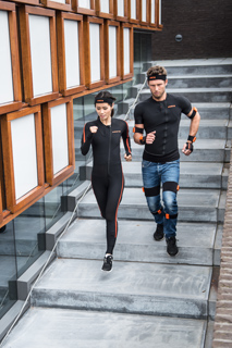 A man and a woman in black athletic suits with orange sensors run up concrete stairs.