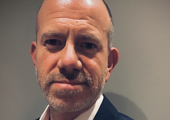 Close-up portrait of a middle-aged man with short hair, a beard, and a light-colored shirt.