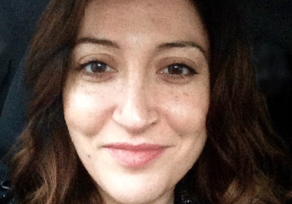 A close-up portrait of a woman with brown hair and a slight smile.