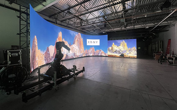 A large curved LED screen showing a mountain range in a dark studio with camera equipment.