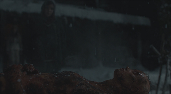 A person's body lies face up in the snow during a dark, snowy night.