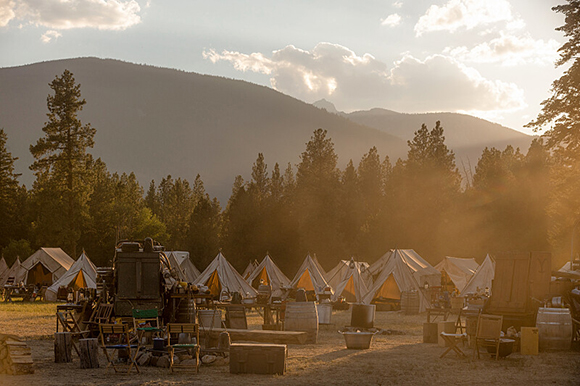 White canvas tents in a mountain valley campsite during a golden sunset.