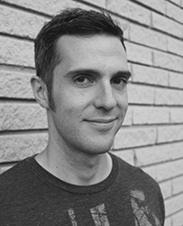 Black and white headshot of a man smiling slightly in front of a brick wall.