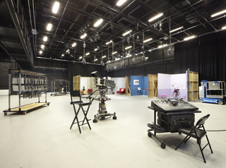 A large, empty film studio with lighting rigs, cameras, production equipment, and set pieces.