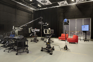 A television studio containing multiple professional cameras on dollies, studio lights, and a monitor.